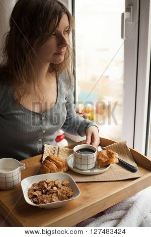 Healthy breakfast in bed served on tray with coffee, cornflakes, croissant and milk. Woman having her breakfast in bed.
