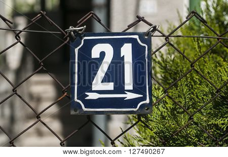 Weathered grunge square metal enameled plate of number of street address with number 21 closeup