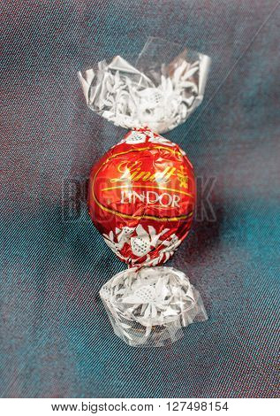 KILCHBERG SWITZERLAND - MARCH 20 2014: Lindt Lindor chocolate truffle on a chameleon luxury silk background. Lindt is one one of the lastgest luxury chocolate and confectionery company worldwide with more than 30 factories worldwide