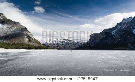 Alone woman on a frozen lake with Rocky Mountains in background, Banff National Park, Alberta, Canada