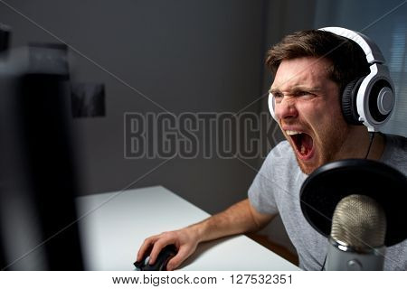 technology, gaming, entertainment, let's play and people concept - angry screaming young man in headset with pc computer playing game at home and streaming playthrough or walkthrough video