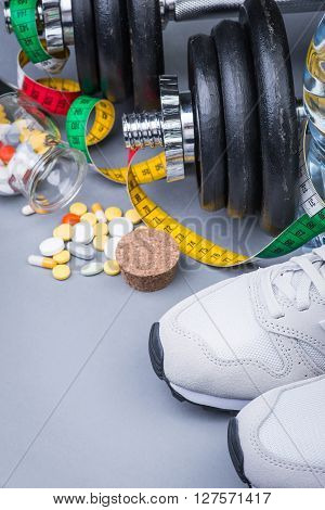 Dumbbells with measuring tape trainers pills and bottle of chilling water on grey