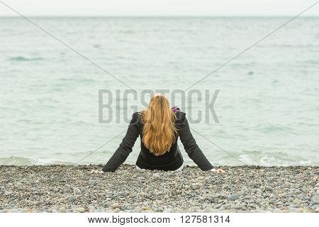 She Sits Back On A Pebble Beach By The Sea On A Cloudy Day, His Head Thrown Back