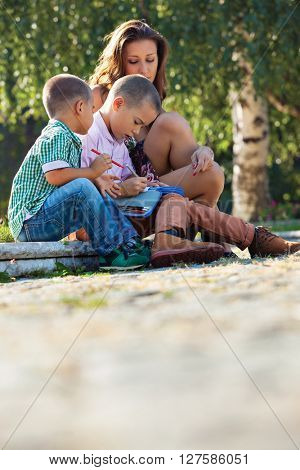 Back to school - two  little boys studying lesons in the summer or spring park with their mother.