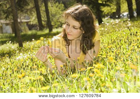 Yount woman lays on meadow with yellow dandelions