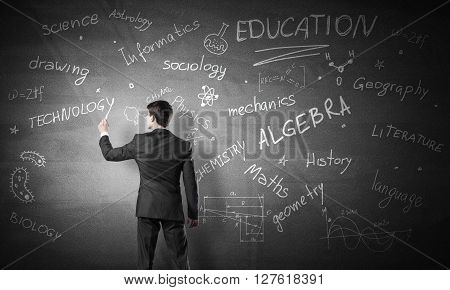 Rear view of man drawing education concept on blackboard with chalk