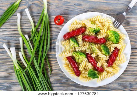 Delicious Spiral Pasta salad with broccoli and grilled sausages decorated with dill on a white dish with tomato sauce in a gravy boat studio lights top view