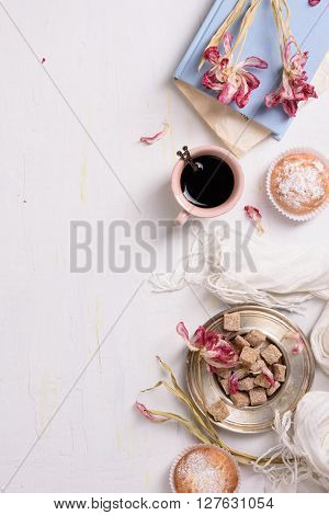 Coffee and vanilla cupcakes with pink tulip flowers over white background, top view.