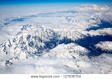 Snow covered mountains and rocky peaks in the French Alps, over blue sky. View from airplane