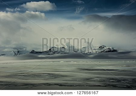 Myterious mountain panorama behind frozen foggy glacier lake