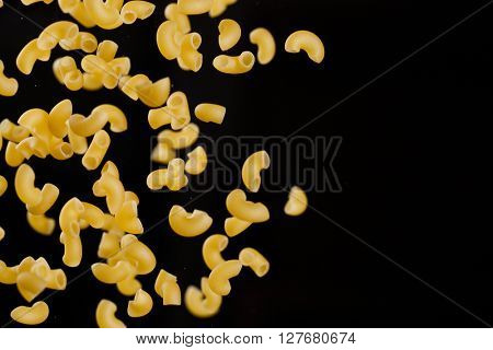 Falling gobetti pasta. Flying yellow raw macaroni over black background. 