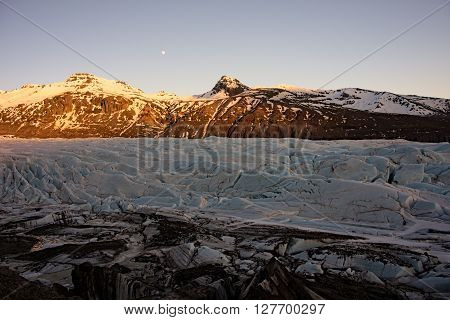 Offshoots of a glaciers tongue in front of mountains in iceland with moon
