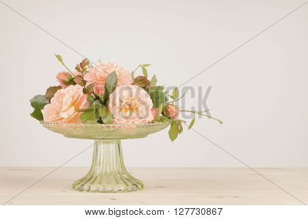 Old fashioned pink roses arranged in a green glass vase. Colors muted and vignette added with photographic filter.
