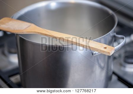 Wooden spoon over a hot metal pot while cooking a meal on a gas stove. Selecive focus.