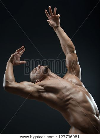 Bodybuilder and strip theme: beautiful with pumped muscles naked man posing in the studio on a dark background shot