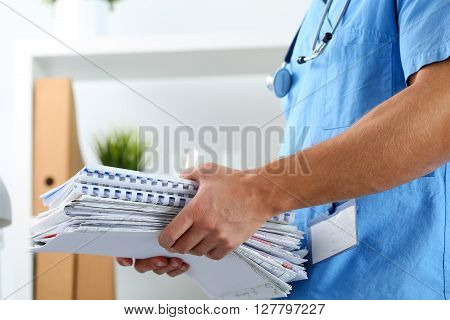 Hands of medicine therapeutist doctor wearing blue uniform holding pile of business papers at work table. Medications consumption account, bureaucracy in hospital work, patient documentation concept