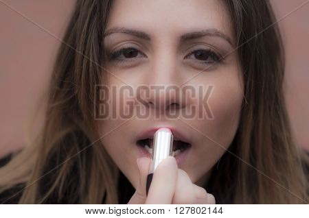 Girl paints her beautiful lips with red lipstick.
