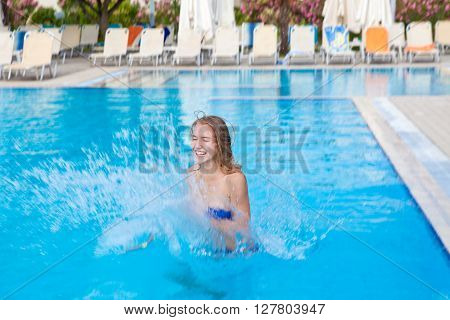 Happy young girl splashing in the pool on a summer's day holiday
