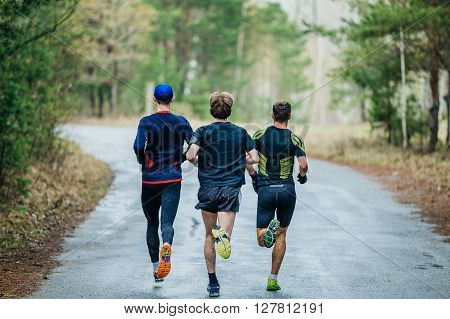 runners three men running down road in woods. feet in a spray of dirt