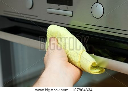 Man's hand wipes a kitchen stove handle.