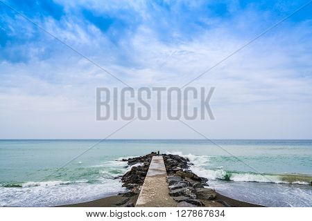Concrete pier or jetty on seascape with cloudy blue sky in Levanto Italy