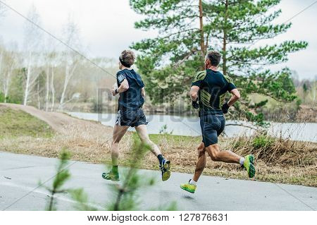 two leading athletes runners running down road in Park past lake