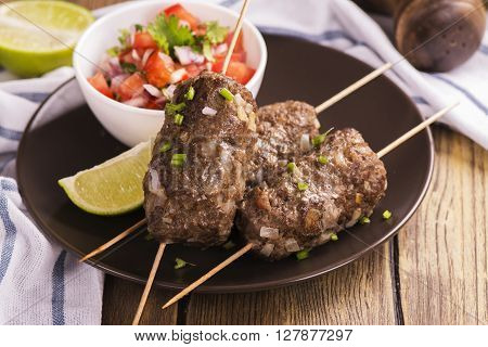 Grilled kebabs with vegetable salad and seasonings over wooden table