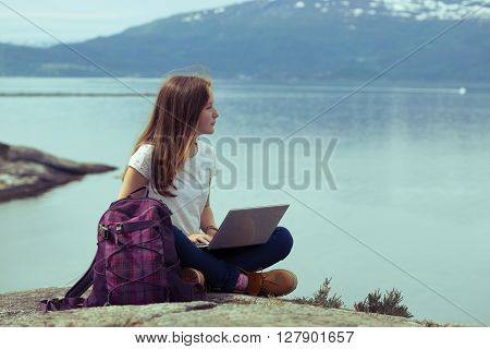 girl hiker with a laptop sitting on a rock on a background of mountains and lakes norway