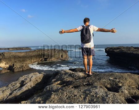 Man on the edge of a cliff, stone beach landscape, sea panorama, stone and rocks on the beach, happy man on beach, free man by sea, summer holiday freedom, wild beach and sea waves, Bali, Indonesia