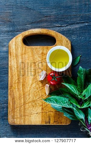 Fresh butch of thai basil and tomatoes with olive oil on rustic wooden cutting board over dark background top view. Vegetarian food cooking concept.