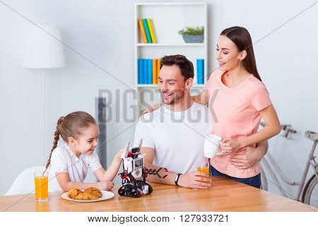 Feel support. Cheerful nice couple embracing and sitting at the table with their daughter while having a meal