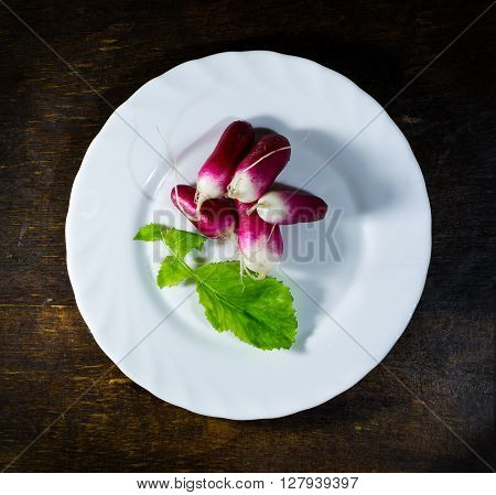 Fresh radishes in white plate on old wooden table