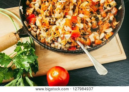 Cooked vegetables and mushrooms in frying pan with red tomato and green leaf