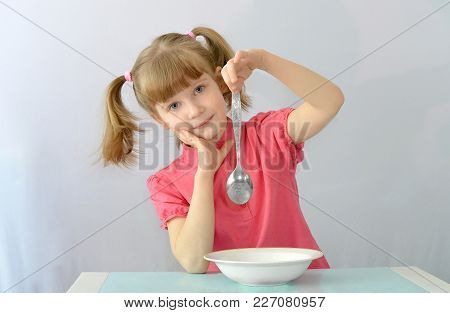 child, kid,left-handed sitting at table holding spoon with the left hand.