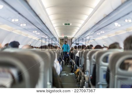 Interior Of Commercial Airplane With Flight Attandant Serving Passengers On Seats During Flight. Ste