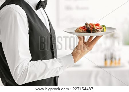 Waiter holding plate with meat and vegetables, closeup