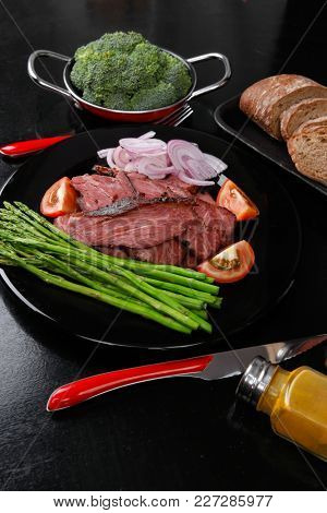 business lunch fresh roast beef meat slices on black plate wotj cutlery asparagus boiled broccoli rye bun on wooden table