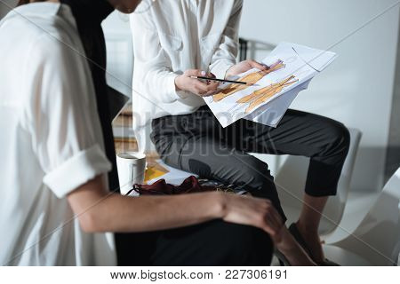 Croped Shot Of Fashion Designers Sitting On Table And Discovering Sketches