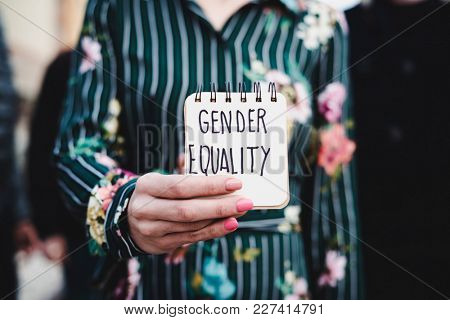 closeup of a young woman outdoors showing a notepad in front of her with the text gender equality written in it