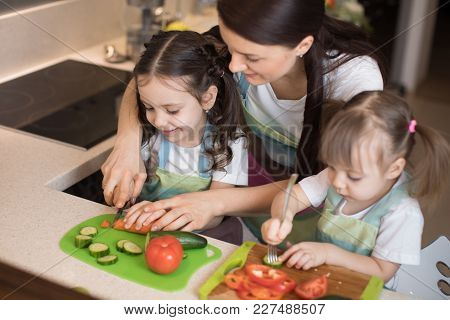 Mum Chopping Vegetables With Two Kids Daughters In Family Home Kitchen.