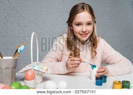 Dorable Happy Girl Painting Easter Egg And Smiling At Camera
