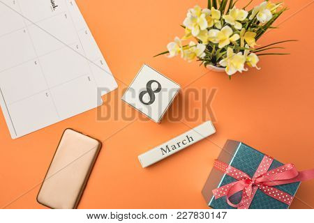 The Top View Of Orange Desk With Phone, Gift, Flowers And Notebook