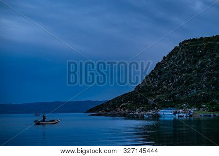 Aymara Man Paddling And Fishing In A Small Boat In The Picturesque Challa Bay Located In The Famous 