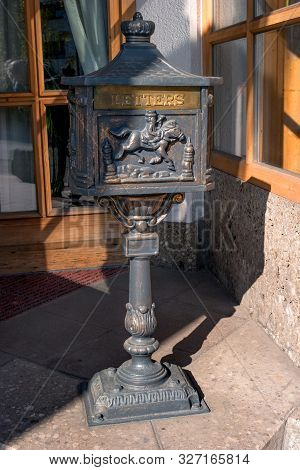 Old Black Metal Mailbox On A Metal Base. The Bas-relief Is Made On The Box - The Postman On A Horse 