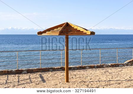 Parasol Close-up On The Beach Of Lake Issyk-kul With Snow-capped Mountains On The Horizon. Kyrgyzsta