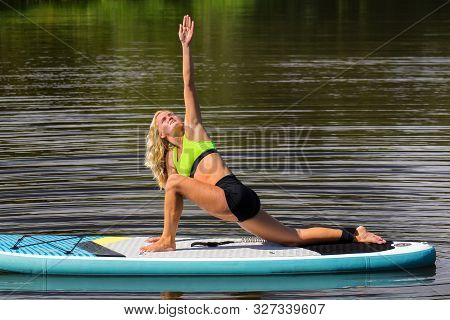 Young European Woman In Triangle Pose On Floating Paddle Board