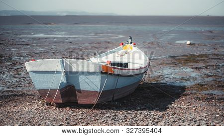 Rearview Of An Old Colorful Painted Wooden Rope-bound Fishing Boat On The Pebble Of The River Bank W