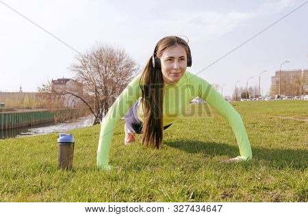 1 White Woman Doing Push Ups On The Grass By The River In The City, Workout
