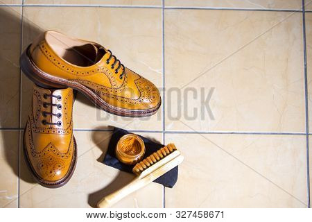 Pair Of Luxury Male Full Brogued Tan Oxford Shoes. Placed Together With Shoe Wax And Brush On Tiles 