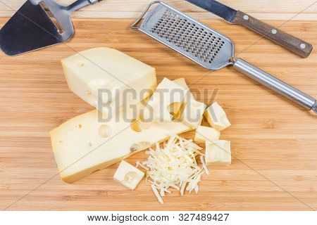 Top View Of Partly Sliced And Grated Swiss-type Cheese On A Bamboo Wooden Cutting Board Against Of C
